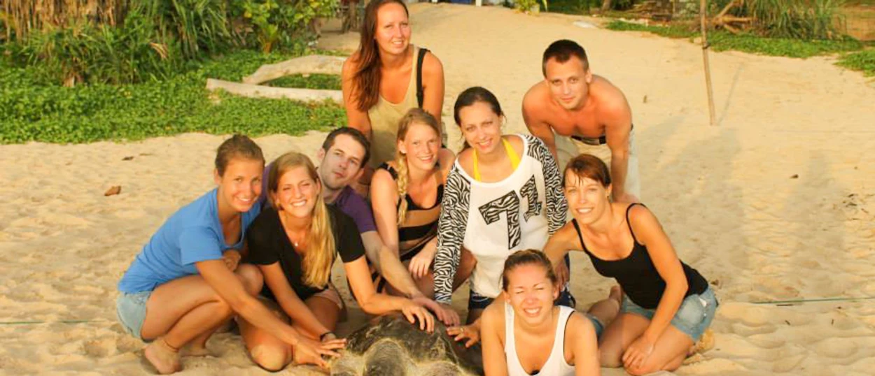 A group of happy young volunteers gathered around a sea turtle on the sandy beach in Sri Lanka.